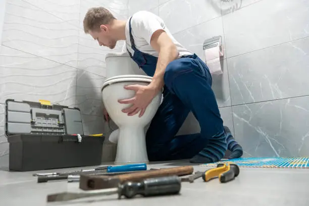 A professional plumber inspecting a toilet base and bathroom piping as part of a residential plumbing checklist in Oklahoma City.
