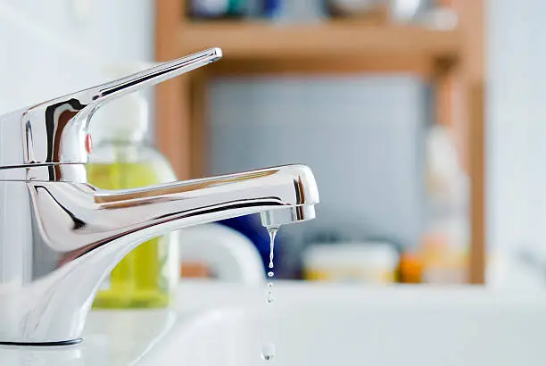 Close-up of water dripping from a chrome bathroom tap spout, illustrating how much water a small leak actually uses.