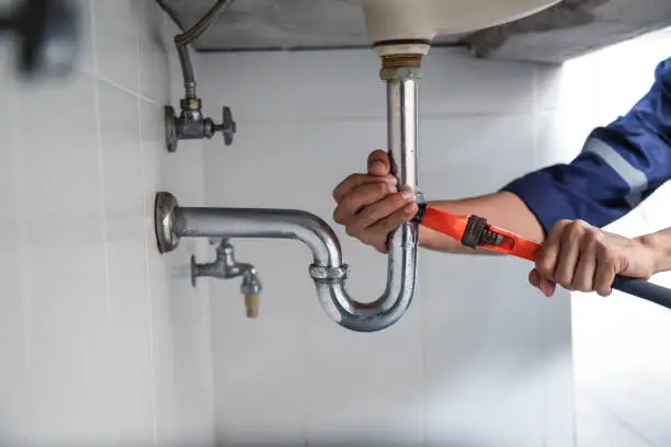 Professional plumber checking indoor pipe fittings and connection points for stress leaks.