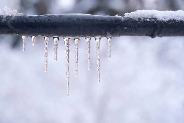 Outdoor exposed plumbing pipe covered in snow with hanging icicles during severe freezing winter weather in Oklahoma.