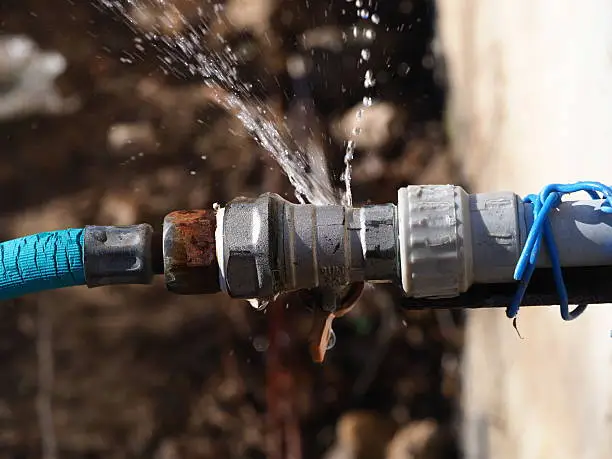 High-pressure water spraying from a cracked pipe connection outdoor, indicating joint strain.