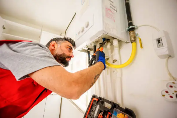 A plumber using a wrench to inspect a tankless water heater as part of a home plumbing checklist in OKC.