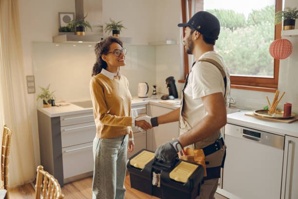 > A friendly, professional plumber in Oklahoma City shaking hands with a smiling homeowner in her kitchen while holding a tool chest, representing dependable, local plumbing services ready to repair soil-related pipe issues.
