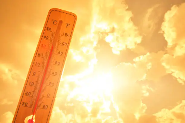 Outdoor thermometer showing high temperature under a bright, glaring sun and hazy sky during extreme weather.