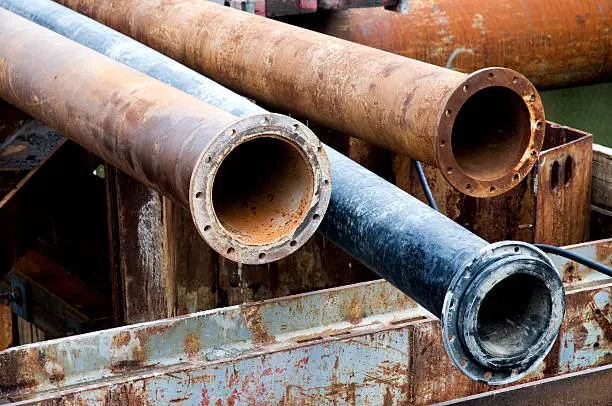 Old rusted heavy metal water service line pipes lying outdoors.