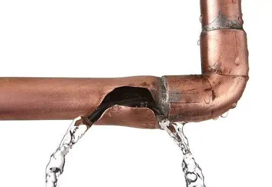 Burst copper pipe leaking water from a rupture near an elbow joint.