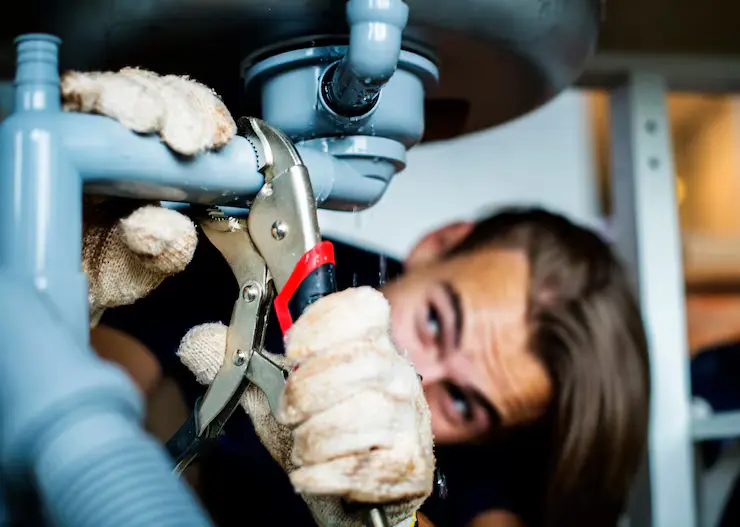 Plumber using locking pliers to tighten a drain pipe under a sink during sewer repair.