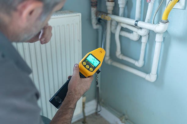 Plumber using electronic leak detection device on indoor plumbing pipes.