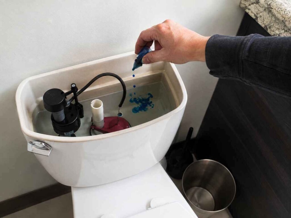 Blue dye being added to an open toilet tank to check for a silent toilet leak that may increase household water usage.