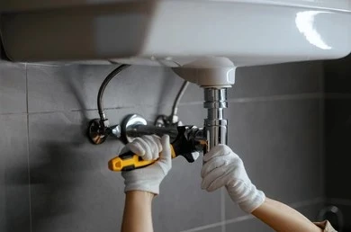 Plumber repairing pipes under a bathroom sink for Oklahoma rental plumbing laws blog post.