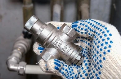 Plumber holding a 1/2 inch brass water pressure regulator valve in a gloved hand.