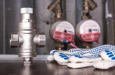 Brass water pressure reducing valve (PRV) sitting next to work gloves and water meters.