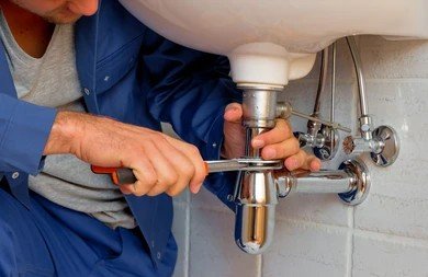 Plumber using a wrench to repair sink pipe plumbing under a bathroom sink.