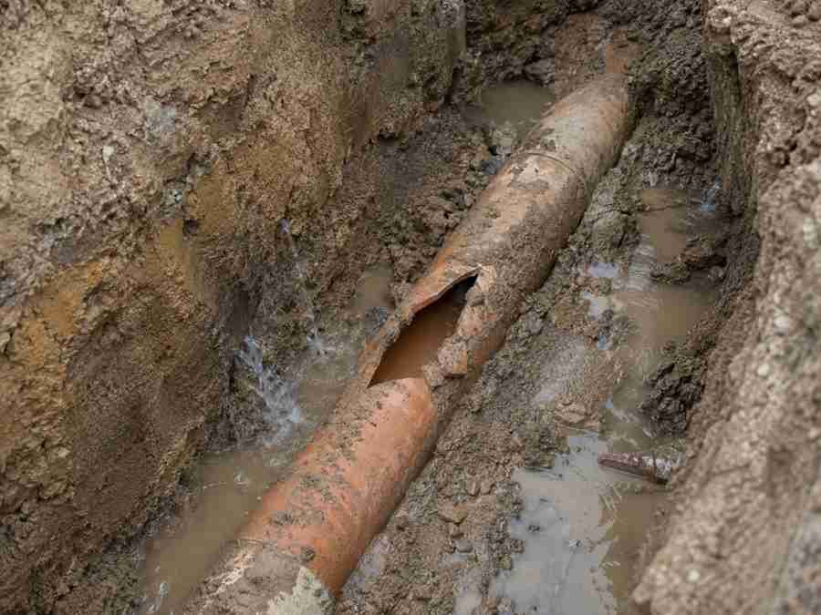 Cracked and broken underground sewer pipe leaking in a muddy trench.
