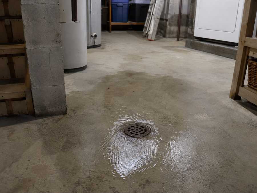 Water backing up and flooding concrete floor around a basement drain.