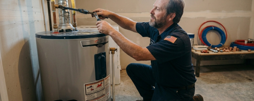 Experienced plumber tightening utility line connections on top of a residential gas water heater tank during a repair service in Oklahoma City, OK.